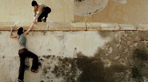 A young man helping a young women to pass over a wall